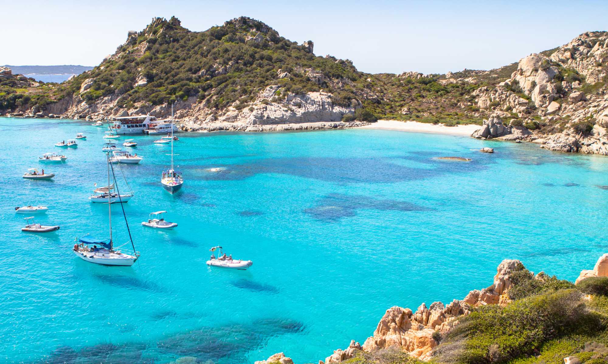 Caletta cristallina in Sardegna, circondata da rocce e vegetazione, rappresenta un paradiso nascosto.